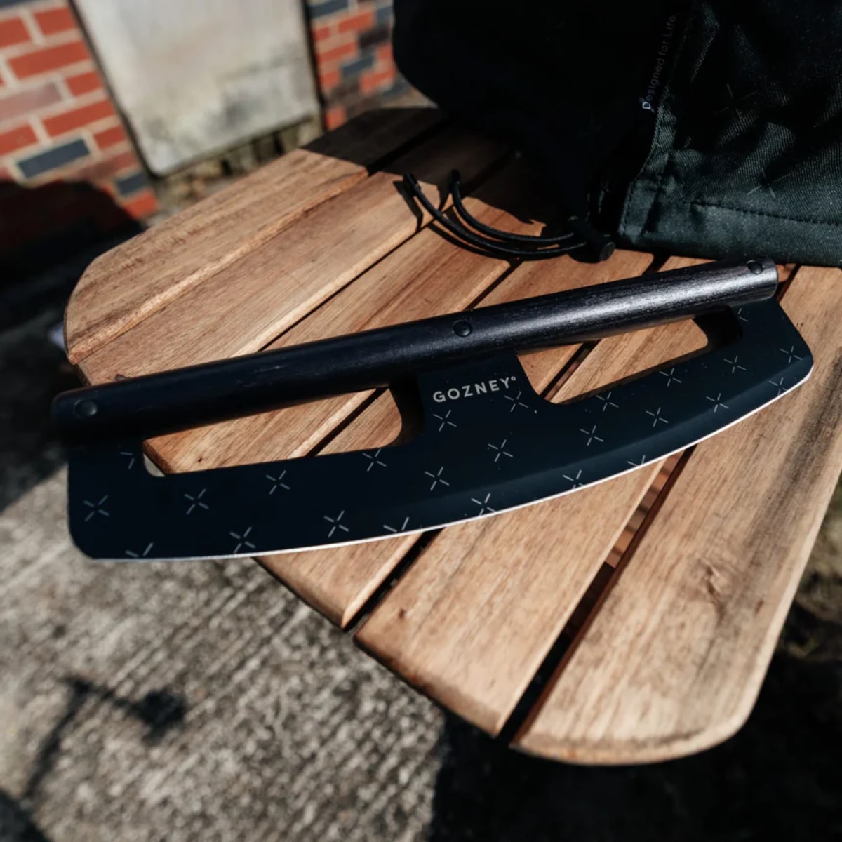 Gozney Pizza Rocker knife with a curved blade for easily slicing pizza, shown on a wooden surface.